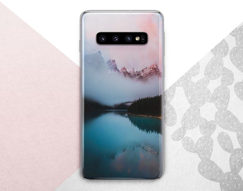 Pu&ograve; includere: Una custodia per telefono trasparente con un'immagine panoramica di una catena montuosa riflessa in un lago. L'immagine &egrave; di un blu e un grigio morbidi e tenui con un tocco di rosa nel cielo.