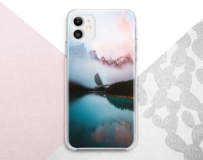 Pu&ograve; includere: Una custodia per telefono trasparente con un'immagine panoramica di un lago di montagna e montagne innevate sullo sfondo. Il cielo &egrave; di un rosa e un arancio tenue.