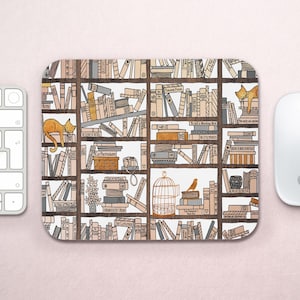 May include: A white mouse pad with a repeating pattern of bookshelves filled with books, a bird in a cage, and orange cats. The bookshelves are brown and the books are various colors. The text on the books includes titles like "Paradise Found", "The Little Prince", and "To Kill a Mockingbird".