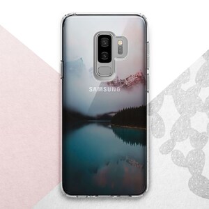 Pu&ograve; includere: Una custodia per telefono trasparente con un'immagine di paesaggio di un lago e montagne. La custodia ha un logo Samsung sul retro.