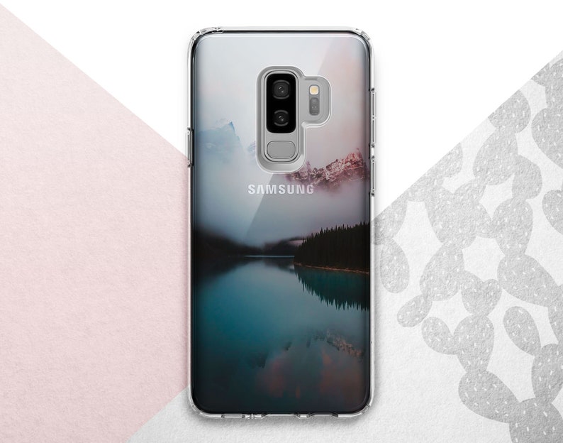 Pu&ograve; includere: Una custodia per telefono trasparente con un'immagine di paesaggio di un lago e montagne. La custodia ha un logo Samsung sul retro.