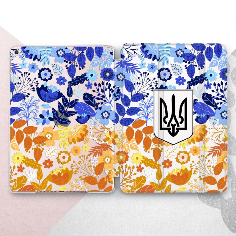 Peut inclure: &Eacute;tui pour tablette &agrave; motifs floraux bleus, oranges et blancs. Il pr&eacute;sente un &eacute;cusson blanc avec un embl&egrave;me de trident noir. L'&eacute;tui est ouvert, r&eacute;v&eacute;lant l'int&eacute;rieur.