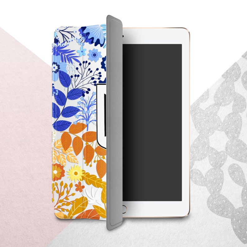 Peut inclure: Une tablette blanche avec un &eacute;cran noir, partiellement recouverte d'un &eacute;tui &agrave; motifs floraux. L'&eacute;tui pr&eacute;sente un motif de feuilles et de fleurs bleues, oranges et jaunes. La tablette est sur un fond blanc et rose.