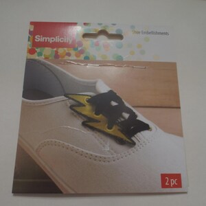 May include: A package of Simplicity shoe embellishments featuring a white shoe with a black and yellow lightning bolt design. The package includes the text "Simplicity" and "2 pc".