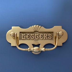 May include: A gold-toned door knocker with a decorative design and the word "LETTERS" engraved on the front.