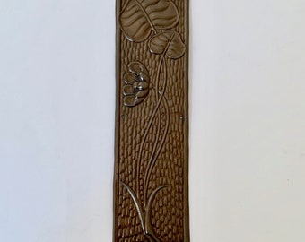 May include: A brown metal door plate with a raised design of a flower and leaves. The plate has a textured background.