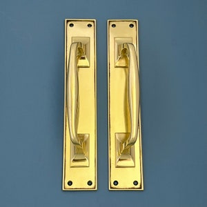 May include: Two polished brass door handles with a simple, elegant design. The handles are rectangular with a curved, D-shaped pull.