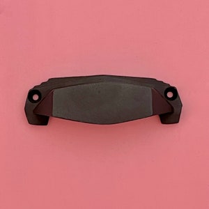 Può includere: Una maniglia per cassetto in metallo nero con un design geometrico. La maniglia ha una forma leggermente curva e una finitura liscia.