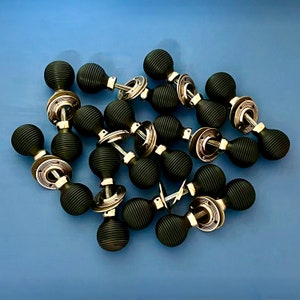 Puede incluir: Una colección de pomos de puerta negros con acabado plateado. Los pomos tienen un diseño decorativo y acanalado.