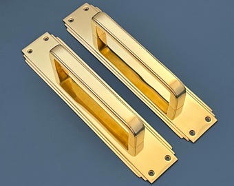 Könnte beinhalten: Zwei goldfarbene Türklinken mit rechteckiger Platte und eingelassenem Griff. Die Griffe haben ein schlichtes, modernes Design.