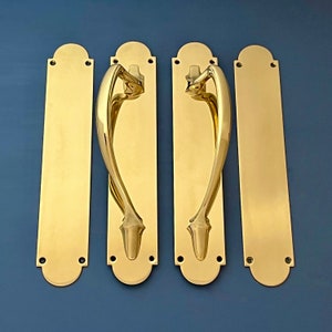 May include: Set of four polished brass door handles with a decorative design. The handles are rectangular with a curved top and bottom. Each handle has a single, curved, decorative pull.