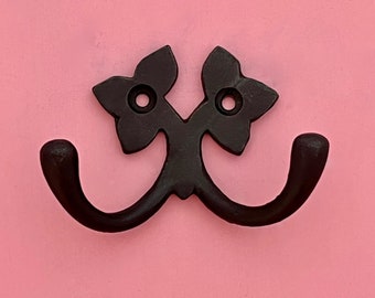 May include: Black metal double hook with a floral design. The hooks are attached to a wall.