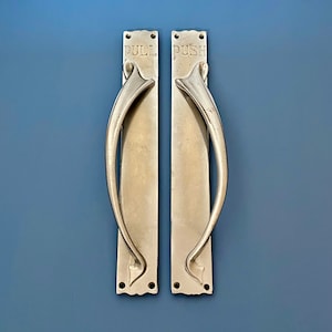 May include: Two silver door handles with ornate designs. The left handle says "PULL" and the right handle says "PUSH".