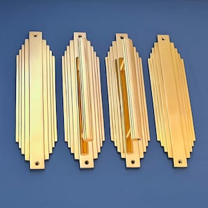 Op de afbeelding: Vier goudkleurige metalen deurgrepen met een Art Deco-ontwerp. Elke greep is rechthoekig met een verticale groef in het midden.