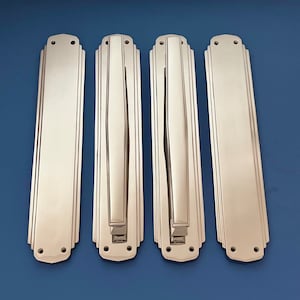 Puede incluir: Cuatro tiradores de puerta de plata pulida con un diseño Art Deco. Cada tirador tiene una placa rectangular con una barra curva en relieve.