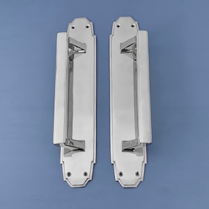 Peut inclure: Deux poignées de porte en chrome poli de forme rectangulaire avec un design décoratif. Les poignées ont un bord surélevé et une surface lisse.