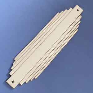 May include: A silver-coloured metal door handle with a geometric design. The handle is made of multiple thin strips of metal that are arranged in a fan shape. The handle has two small holes for screws.