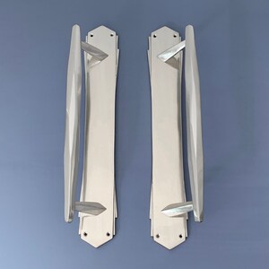 Peut inclure: Deux poignées de porte argentées avec un design géométrique. Les poignées sont longues et étroites avec une extrémité pointue. Elles sont en métal et ont une finition polie.