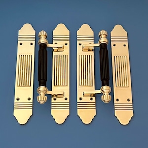 Puede incluir: Conjunto de cinco tiradores de puerta de color dorado con detalles negros. Cada tirador presenta una placa rectangular con líneas verticales y una parte superior decorativa. Los tiradores tienen un diseño de palanca con un pomo negro.