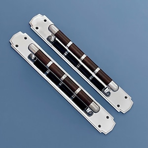 Puede incluir: Dos manijas de puerta plateadas con detalles en marrón oscuro y negro. Las manijas tienen forma rectangular con extremos redondeados y están montadas sobre un fondo azul. Las manijas tienen un diseño decorativo.