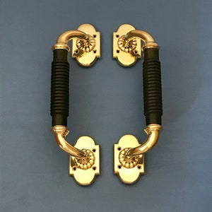 May include: A pair of black and gold door handles with a decorative design. The handles are made of metal and have a black rubber grip.