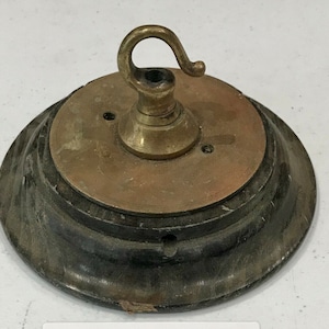 Könnte beinhalten: Eine antike Deckenleuchte aus Messing mit einem Haken und einem Holzsockel. Die Leuchte hat einen abgenutzten, alten Look.