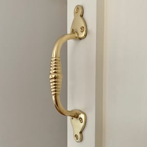May include: A brass door handle with a decorative ribbed design. The handle is attached to a white door.