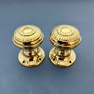 May include: Two gold door knobs with a decorative, fluted design. The knobs have a round shape and a smooth, polished finish.
