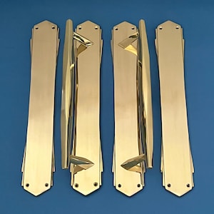 Pode incluir: Quatro puxadores de porta dourados com um design Art Deco. Cada puxador tem uma placa retangular longa com uma pega decorativa curva.