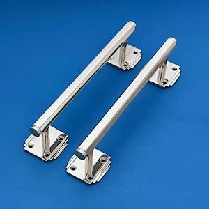 May include: Two polished chrome door pull handles. Each handle has a rectangular base with a series of layered squares and a long, hexagonal bar. The handles are set against a blue background.