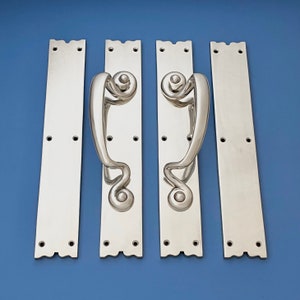 Pode incluir: Quatro maçanetas de porta prateadas com um design decorativo e ornamentado. As maçanetas são montadas em placas retangulares com uma borda ondulada.