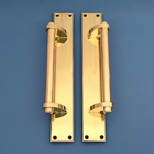 Puede incluir: Un par de manillas de puerta de latón pulido con un diseño cilíndrico. Las manillas están montadas en placas rectangulares con esquinas redondeadas.