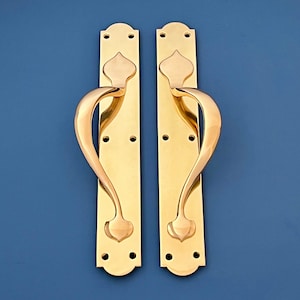 Puede incluir: Un par de manillas de puerta de latón pulido con un diseño curvo decorativo. Las manillas tienen un estilo tradicional y ornamentado.