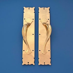 May include: A pair of ornate brass door handles with a decorative floral design. The handles are mounted on rectangular plates with a detailed border.