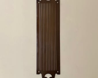 May include: A long, rectangular, brown metal door plate with a decorative, ribbed design and two cut-out handles at the top and bottom.