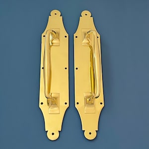 May include: Two gold-toned door handles with a decorative design. The handles are made of solid brass and have a polished finish.