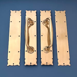 Puede incluir: Tres tiradores de puerta dorados con detalles ornamentados. Cada tirador tiene una placa rectangular y una palanca curva.