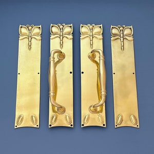 May include: Four brass door handles featuring a butterfly design. The handles are rectangular with a curved bottom. Each handle has a decorative butterfly design at the top and a round knob at the bottom.