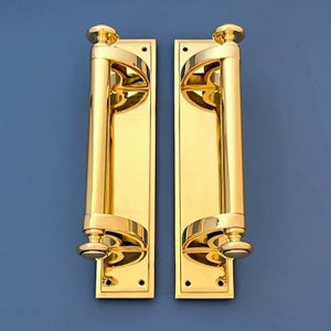 May include: Two polished brass door handles with a decorative design. Each handle has a rectangular backplate and a long, cylindrical lever.