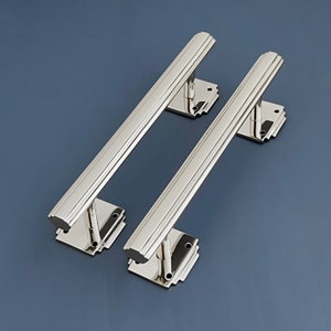 Op de afbeelding: Twee gepolijste nikkel deurgrepen met een rechthoekige vorm en een decoratief ontwerp. De grepen zijn gemonteerd op een vierkante basis met een decoratief ontwerp.