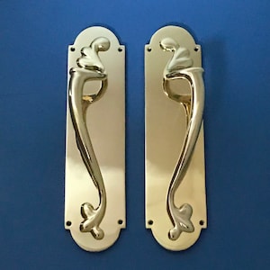 Peut inclure: Une paire de poignées de porte en laiton ornées d'un motif en spirale décoratif. Les poignées sont montées sur des plaques rectangulaires aux bords arrondis.