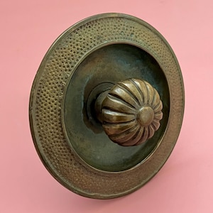 May include: Antique brass door knob with a textured, floral-shaped handle. The knob has a circular design with a dotted border. The metal has a tarnished, aged appearance, suggesting vintage craftsmanship.