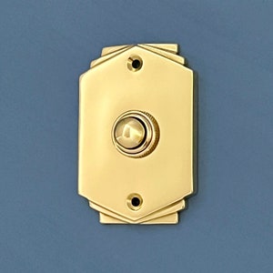 May include: A polished brass doorbell button with a geometric design. The button is round and has a raised edge.