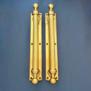 May include: A pair of polished brass door handles with a fluted design and rounded knobs. The handles are mounted on a rectangular plate.