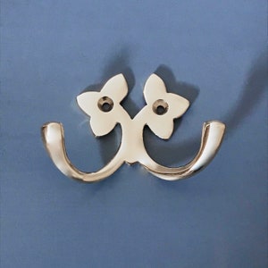 May include: A silver double hook with a floral design. The hooks are curved and have a polished finish.