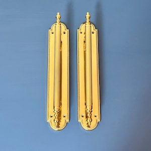 Puede incluir: Dos tiradores de puerta dorados con un diseño decorativo. Cada tirador tiene una forma cilíndrica estriada y un remate decorativo en la parte superior.