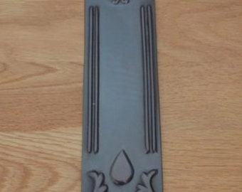 May include: A black metal door plate with an ornate design featuring hearts and leaves. The plate has two holes for mounting.