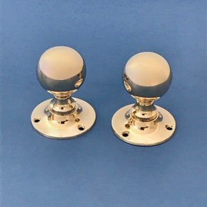 Può includere: Due pomelli per porte in ottone lucido con forma di sfera rotonda e una base circolare con tre fori per viti.