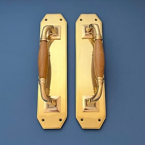 Puede incluir: Dos tiradores de puerta de latón pulido con inserciones de madera. Los tiradores son rectangulares con bordes redondeados y tienen un diseño tradicional.