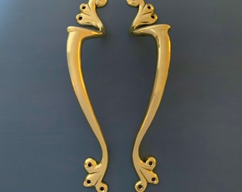 May include: A pair of ornate gold door handles with a decorative, swirling design. The handles have a smooth, polished finish.